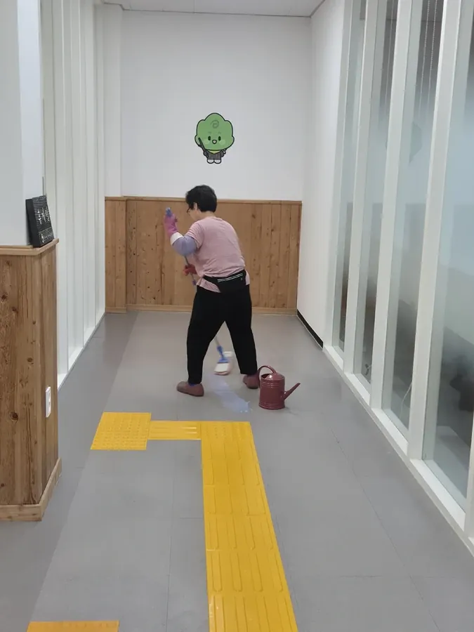 벽면 모서리를 걸레질하는 작업자와 점자유도블록이 깔린 복도
