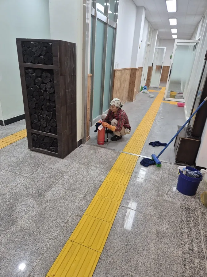 복도에서 소화기를 점검하는 작업자와 점자유도블록
